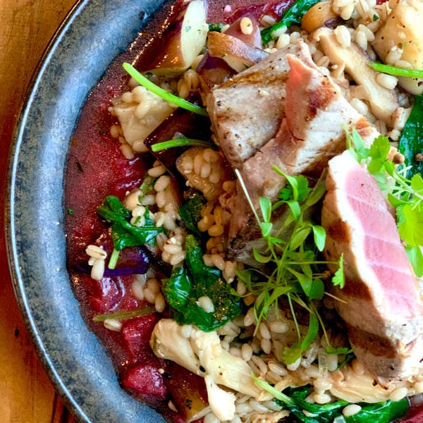 Seared tuna with farro, spinach, mushrooms, and a red sauce, garnished with microgreens.