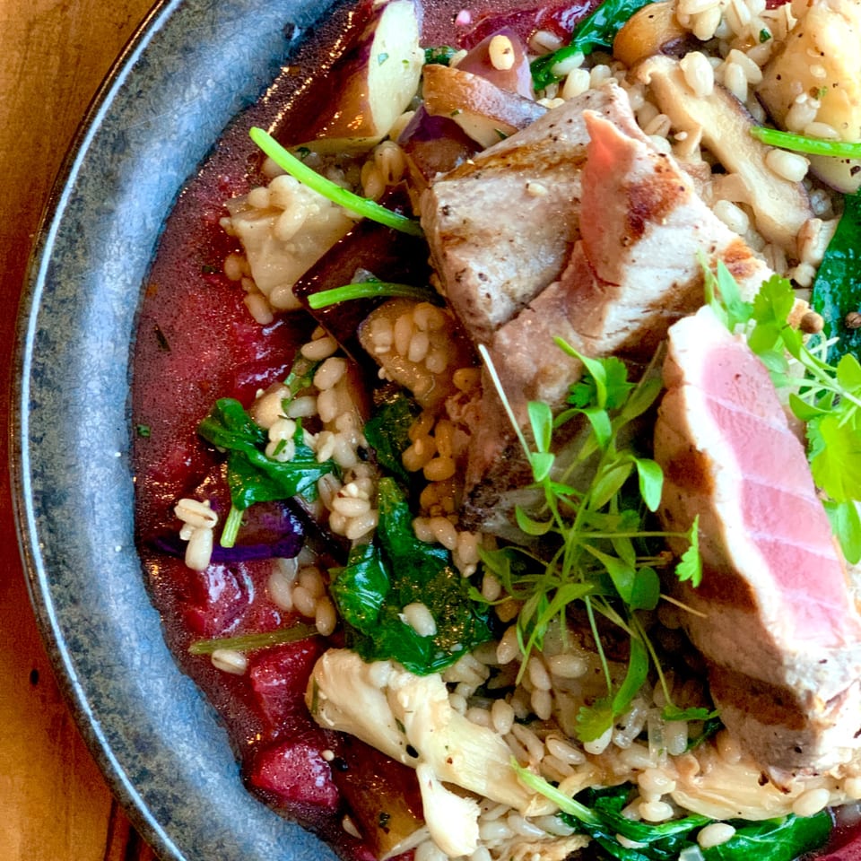 Seared tuna with farro, spinach, mushrooms, and a red sauce, garnished with microgreens.