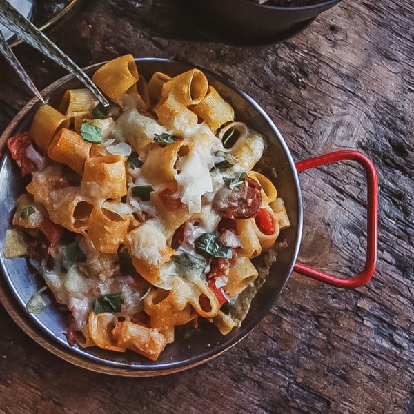 Bandaloop's healthy pasta dish with melted cheese, red peppers, and basil in a metal pan.