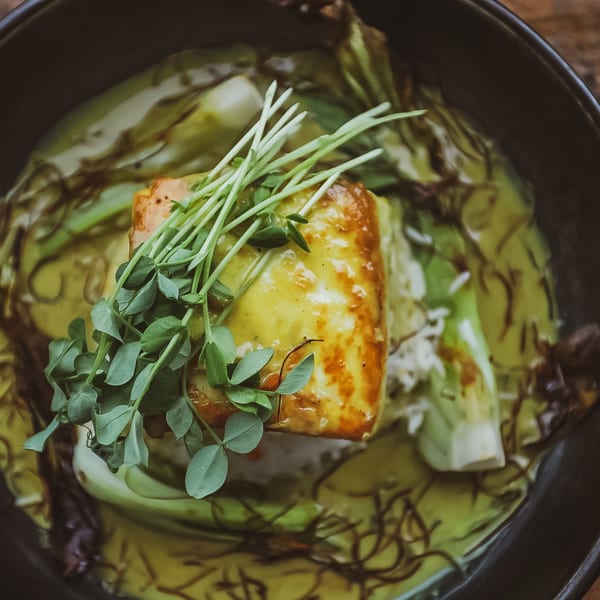 Close-up of Bandaloop's healthy salmon dish with bok choy, rice, and microgreens in a dark bowl.