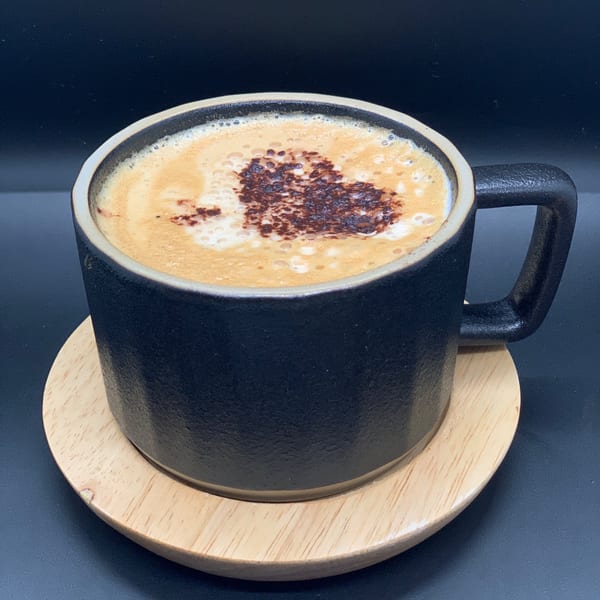 A black mug of Bandaloop coffee with a heart design in the foam sits on a wooden coaster.