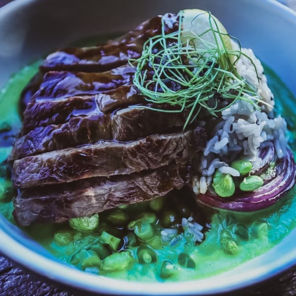 Sliced Bandaloop healthy steak with green sauce, rice, peas, and red onion in a bowl.