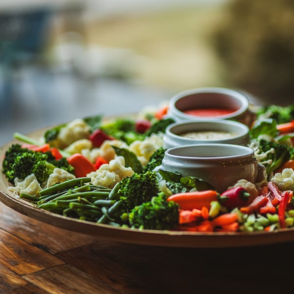 A large platter of fresh, colorful vegetables with three dipping sauces, on a wooden table.
